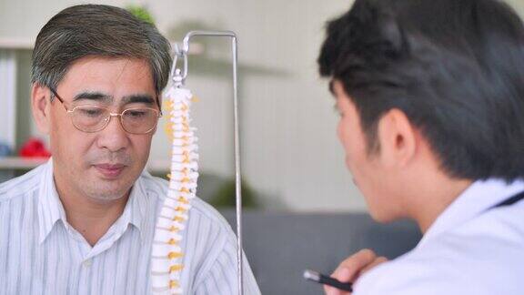 亚洲年轻男性医生向54岁老年男性患者解释脊柱解剖男性医务人员