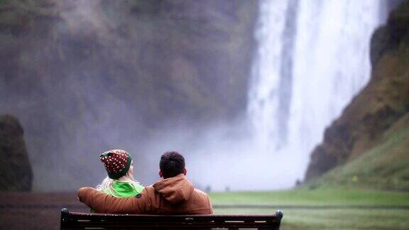 年轻夫妇坐在长椅上欣赏冰岛斯科加佛斯瀑布的美丽景色
