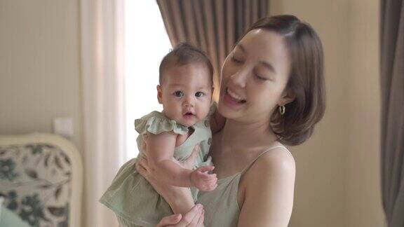 美丽迷人的亚洲妇女的肖像抱着婴儿在卧室附近的窗户在家里短发妈妈抱着宝宝开心的笑30岁的母亲抱着6个月大的婴儿