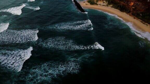 无人机飞过汹涌的海浪到达海岸令人惊叹的蓝色海洋和海滩鸟瞰图
