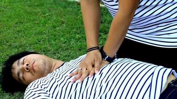 心肺复苏术的急救训练:身穿t恤条纹的男子躺在地上身穿白色长袖衬衫的女子在草地上进行心肺复苏术