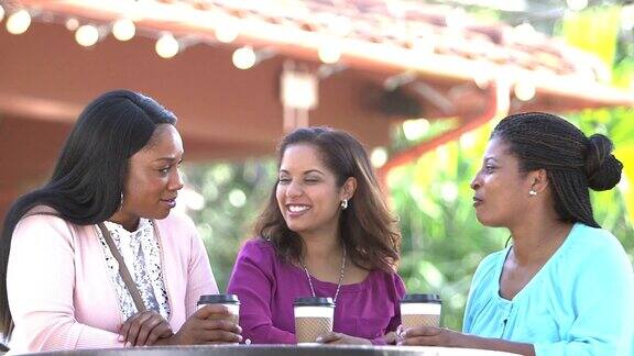 多民族妇女在户外桌子边喝咖啡聊天
