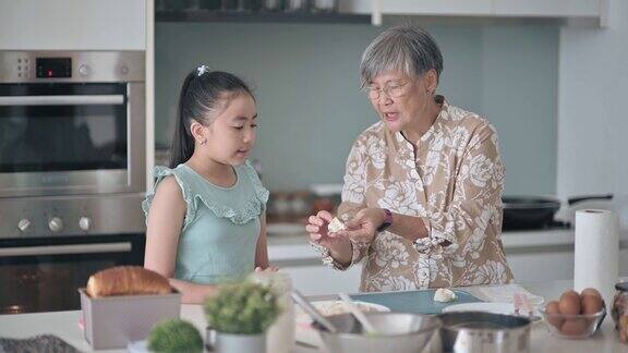 亚裔华人老太太周末在厨房展示和教她的孙女煮饺子