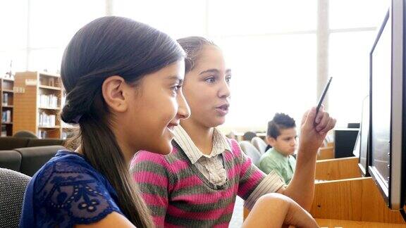 两名西班牙裔少女中学女学生正在STEM学校的图书馆里进行头脑风暴