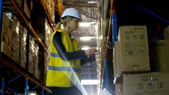 戴安全帽的女性控制器用条形码扫描仪扫描商品她在一个堆满托盘架的大仓库里