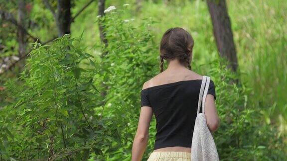 年轻女子在绿色的森林中漫步拿着白色的袋子