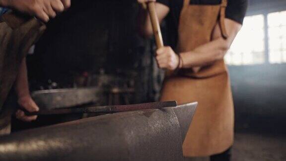 两个铁匠用铁锤在铁砧上敲打一块金属