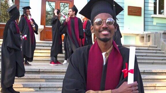 一名男子穿着毕业礼服戴着学士帽手里拿着毕业证书对着镜头微笑