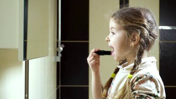 可爱的小女孩在浴室的镜子前涂口红
