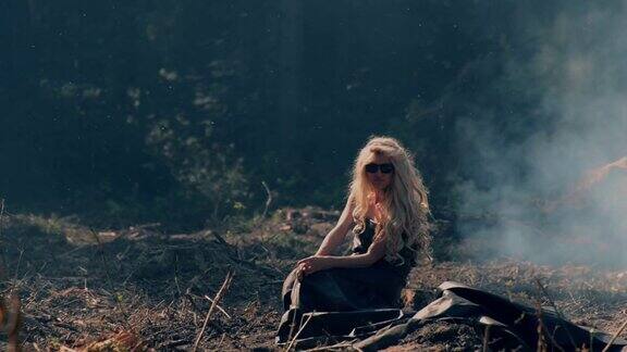 年轻女子坐在燃烧的森林附近的地上