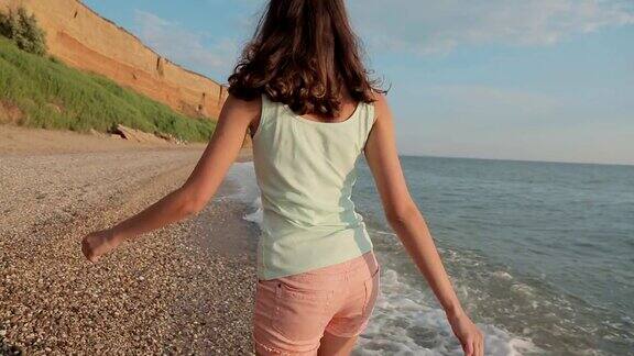 快乐的女孩光着脚在海边的水面上跑着笑着