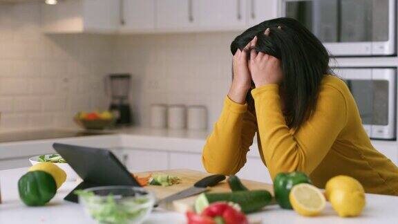 一段4k视频显示一名年轻女子在家里用数码平板电脑做健康食品时看起来很紧张