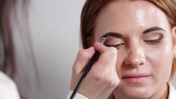 化妆师正在用画笔和阴影在女孩的眉毛上作画