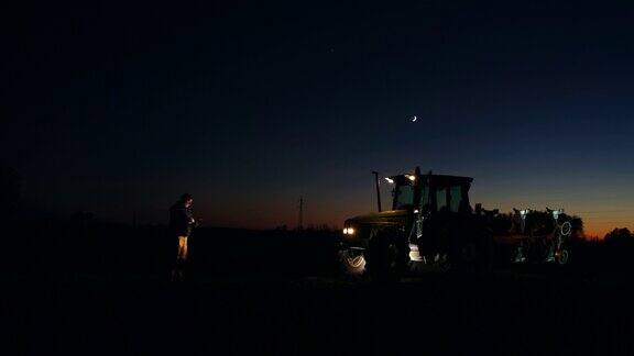 晚上在拖拉机旁使用智能手机的农民