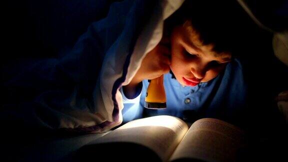 小男孩用手电筒在被子里看书