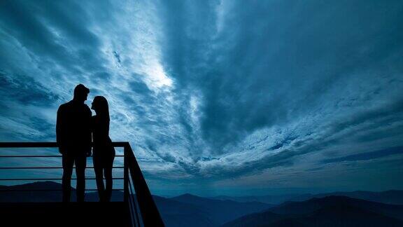 这对情侣站在阳台上夜色衬托着山峦hyperlapse
