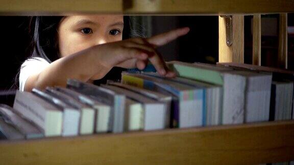 可爱的亚洲小女孩在图书馆的书架上找一本书