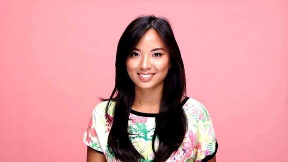 年轻微笑的亚洲女人眨眼在粉红色的背景