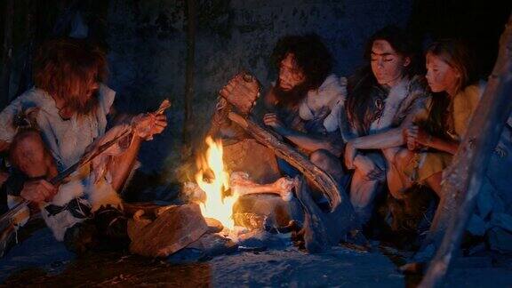 尼安德特人或智人家庭在篝火上烹饪动物肉然后吃它史前狩猎采集者的部落穿着兽皮晚上在洞穴里烧烤和吃肉