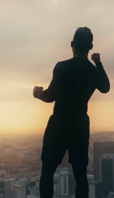 成功的男性运动员在完成健身目标后站在山路上俯瞰城市风景运动男子在他的锻炼中胜利后欢呼和感觉强大