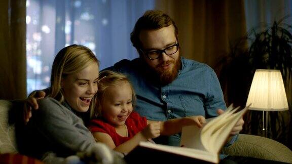 爸爸、妈妈和小女儿在客厅的沙发上读儿童读物这是晚上