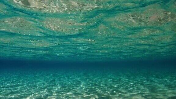 令人惊叹的水下水晶绿松石热带海水与涟漪表面和反射在海底与蓝色背景慢动作