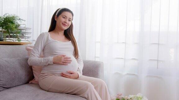 成年孕妇微笑着抚摸自己的肚子在家里