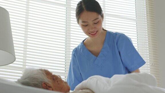年轻的亚洲女性护士护理员养老院的照顾者并在家里用毯子盖住一位年长的亚洲女性