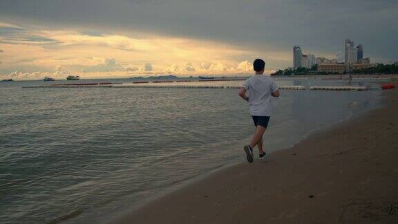 长镜头亚洲运动员在海滩上跑步在一个美丽的日落在夏天
