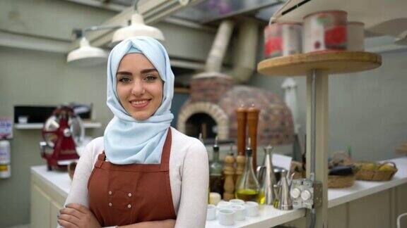 一个美丽的穆斯林妇女的餐馆老板看着镜头微笑着双臂交叉