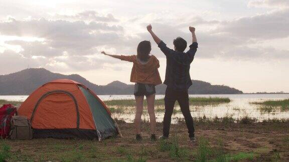 年轻的亚洲露营夫妇在海滩附近的营地跑步和举手