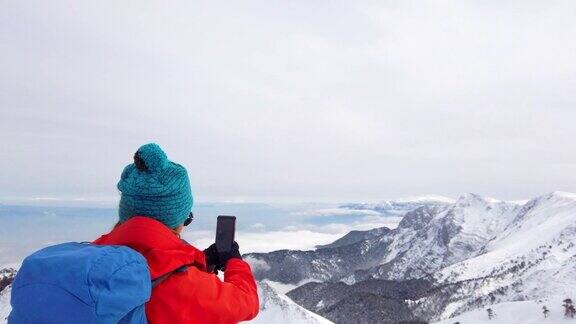 美丽的女性高山登山者用手机在一个高海拔的山峰的顶峰在冬天拍照