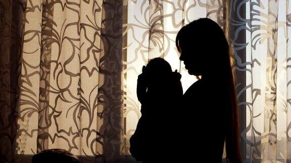 窗前一位年轻母亲带着孩子的剪影在她的怀里摇晃着婴儿在日落时