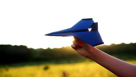 在橙色的夕阳下女人手拿着蓝色的纸飞机自由