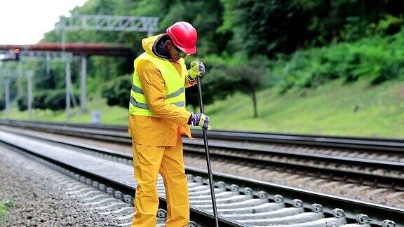 身穿黄制服手拿撬棍的铁路工人正在修理铁轨