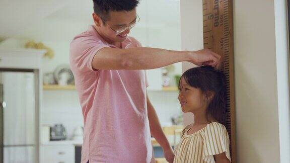 亚洲父亲在家里用墙尺测量踮起脚尖的女儿