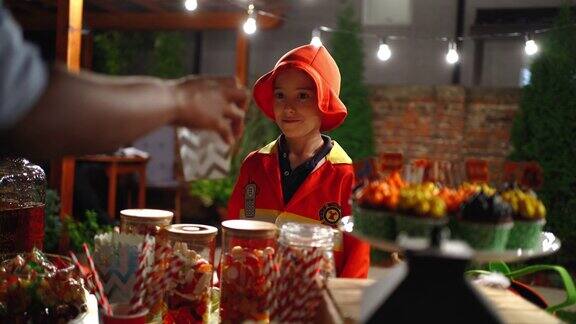 可爱的小男孩穿着消防服在万圣节派对上得到糖果