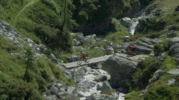 一个成熟的女人男人和年轻的成年男人骑着山地车在一座山河上的木桥上