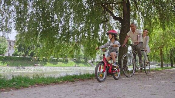 一对夫妇骑着双人自行车他们的小女儿在他们旁边穿过公园
