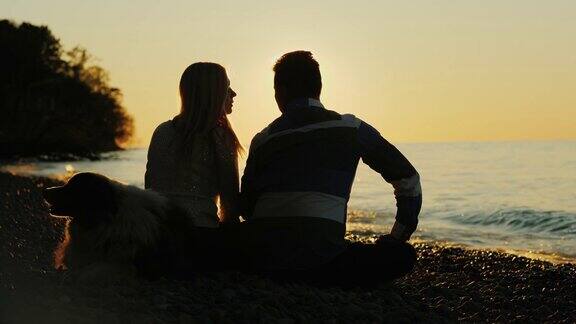一对年轻夫妇带着狗坐在湖边欣赏日落