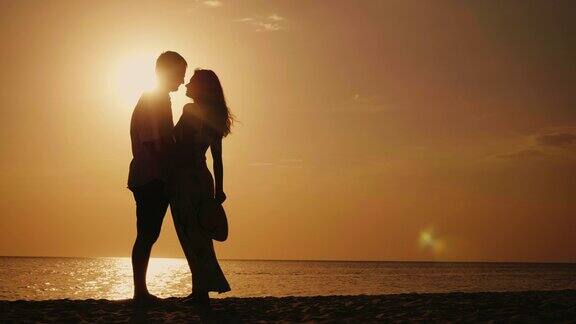 一对相爱的情侣的剪影他们看着对方在日落时拥抱亲吻以大海为背景