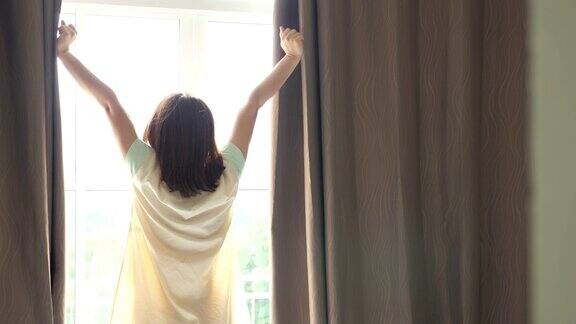 女人打开窗帘和放松在卧室在早晨日出的光线