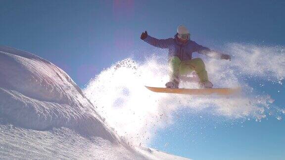 慢动作:专业滑雪板运动员在新雪中跳跃向太阳喷洒雪花