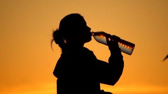 年轻女子在运动后的日落喝水