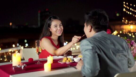 幸福的亚洲夫妇美丽的女人享受晚餐约会与男友在屋顶餐厅浪漫的城市之夜情侣浪漫晚餐和情人节庆祝概念