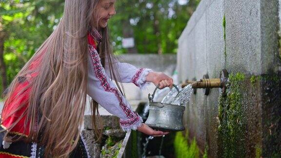保加利亚女孩穿着传统民俗服装斯拉夫民族服装从古老的石头水龙头或喷泉里倒水保加利亚的文化、传统和生活方式
