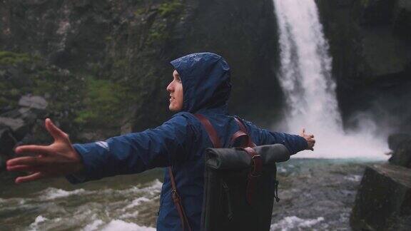 在冰岛的强大瀑布附近一个年轻男子举起双手的背影电影镜头