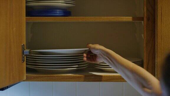 一个白人女人的手把不同大小的盘子放在一个开放式厨房碗柜里