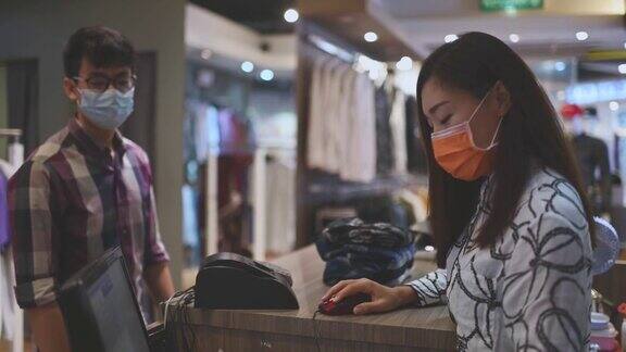 亚洲华人美丽的女男装店店主收银员用口罩折叠衣服她的顾客把他们放在收银台的袋子里
