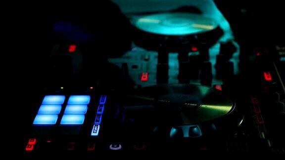 在一个黑暗的夜总会里用数字控制器播放的DJ的手的特写